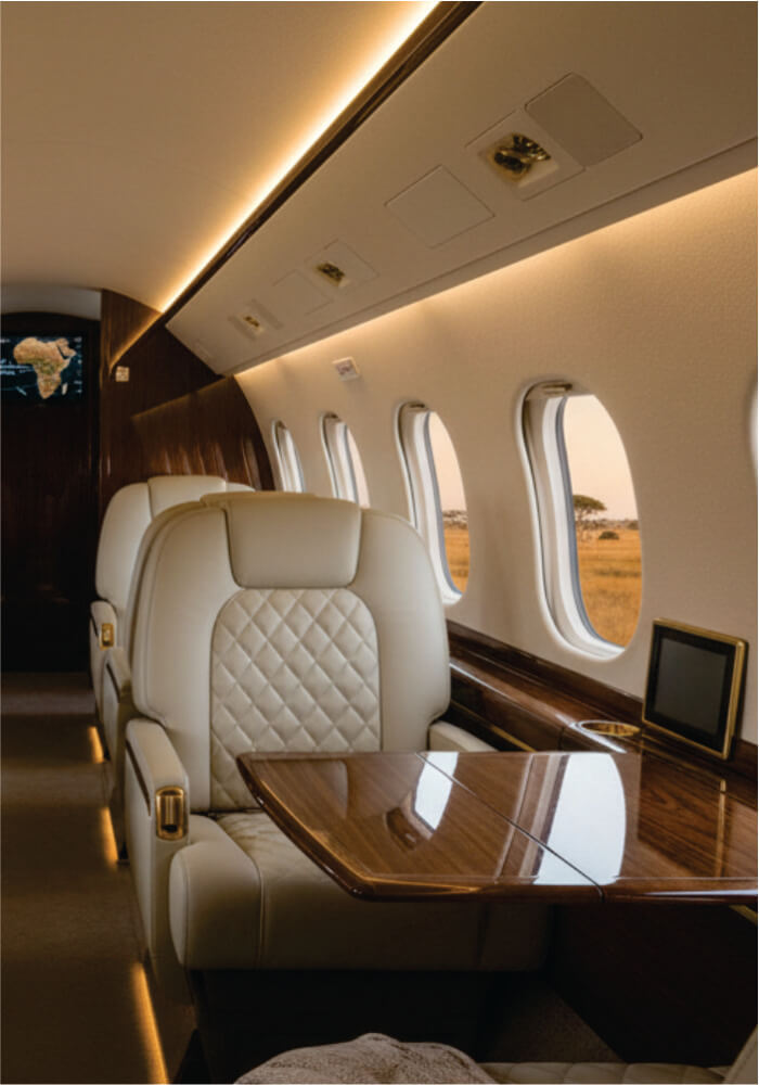 Luxurious interior of a private jet with beige leather seats and a wooden table.