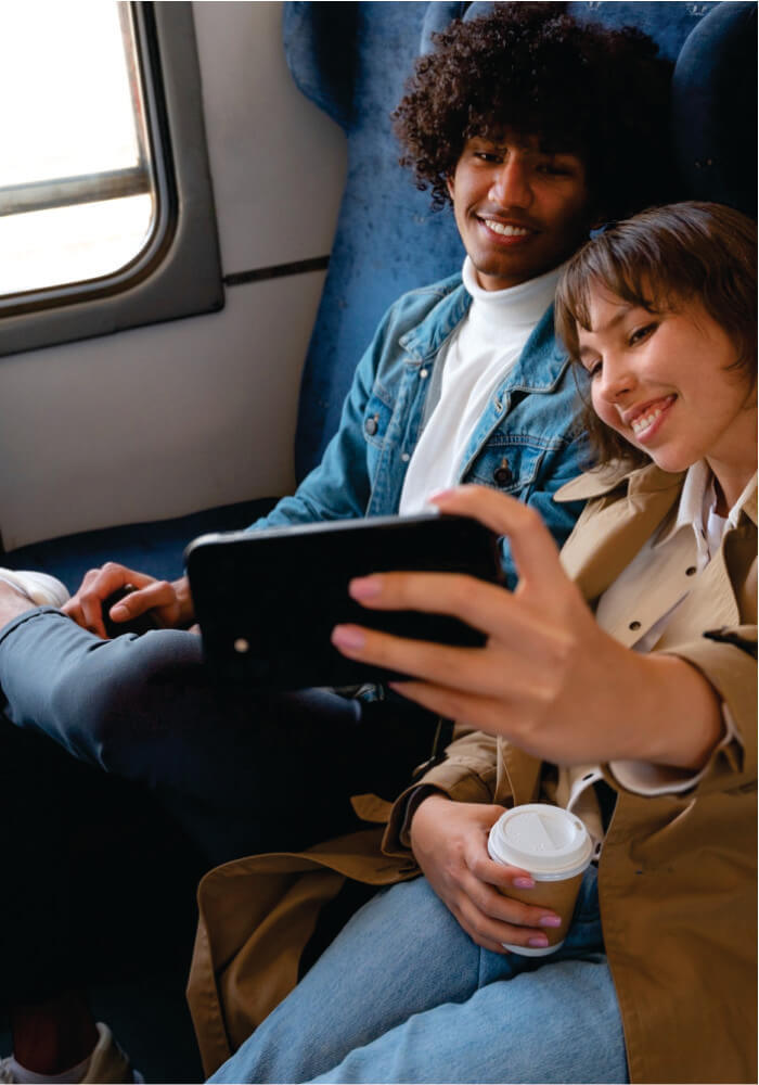 Two people sitting together on a plane, looking at a phone and smiling.