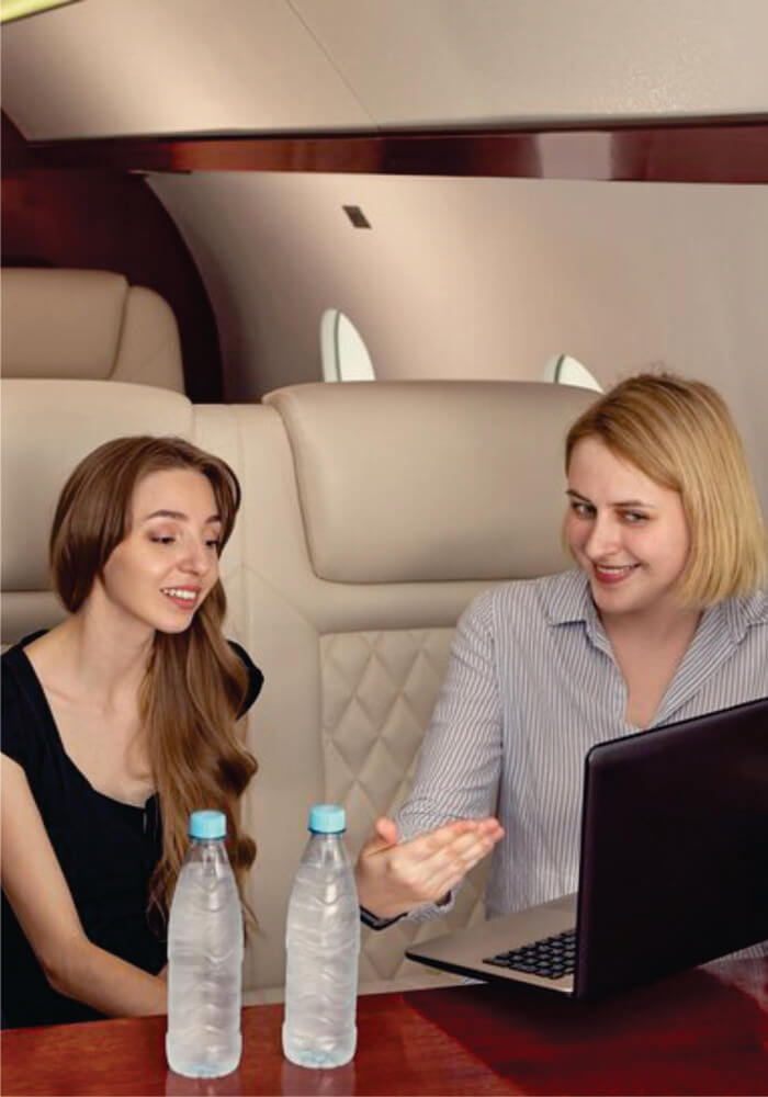 Two rich glamorous women talking while sitting near laptop aboard a private jet on budget Masai Mara fly-in Safari from Nairobi